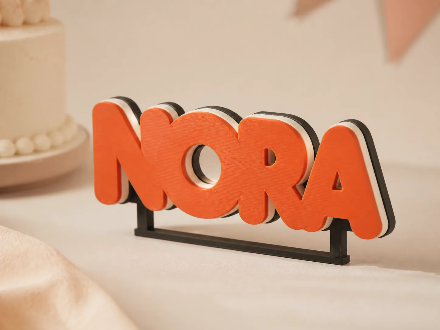 Layered orange NORA name sign with cream and black edges on a warm party table